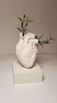 a white heart shaped vase with green stems sticking out of it's back end