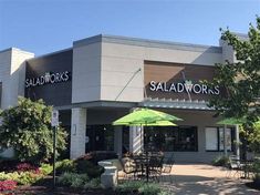 the outside of a salad works restaurant with an umbrella and tables in front of it