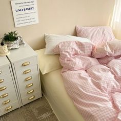 an unmade bed with pink sheets and pillows in front of a white filing cabinet