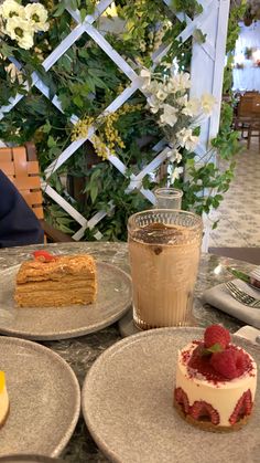 three desserts on plates sitting on a table in front of a vase with flowers