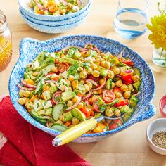 a blue bowl filled with salad next to two bowls of water and flowers in the background