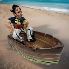 a statue of a man sitting on top of a boat in the sand at the beach