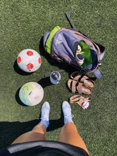 a person's feet and sports equipment sitting on the grass next to a soccer ball