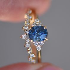 a woman's hand holding a ring with a blue stone surrounded by white diamonds