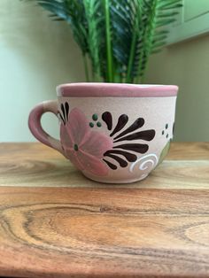 a pink and black coffee cup sitting on top of a wooden table next to a potted plant