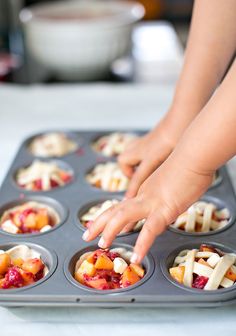 a person reaching into a muffin tin filled with fruit