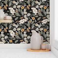 a white vase sitting on top of a counter next to a wallpaper covered in flowers