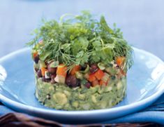 a blue plate topped with a layered guacamole and black bean salad covered in cilantro