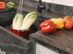 vegetables being washed in a kitchen sink with water running from the faucet over them