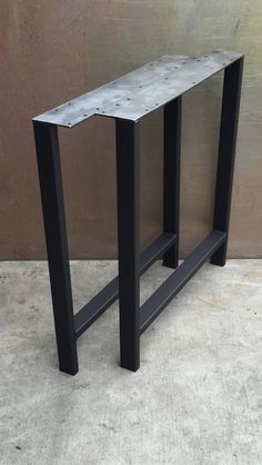 a black metal table sitting on top of a cement floor next to a brown wall