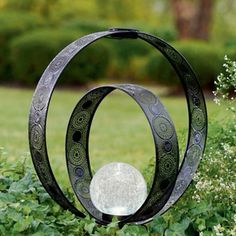 a metal sculpture sitting in the middle of a lush green field next to shrubbery