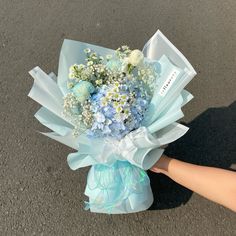 a bouquet of blue and white flowers is being held by someone's hand on the pavement