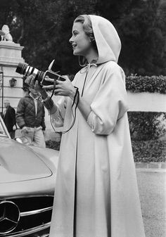 a black and white photo of a woman holding a camera in front of a car