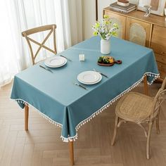 a blue table cloth with tassels and plates on it in front of a window