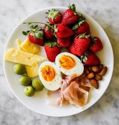 a white plate topped with hard boiled eggs, ham, olives and strawberries