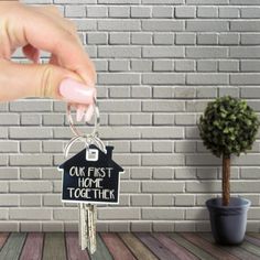 a person holding a house shaped keychain with the words our first home together