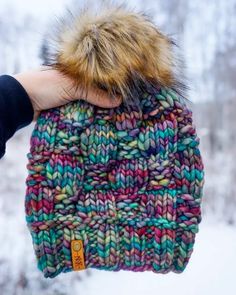 a hand holding a multicolored knit hat with a fur pom