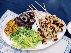 grilled chicken and vegetables on a white plate with blue napkins next to it