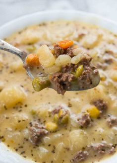 a spoon full of soup with meat and vegetables on it, in a white bowl