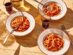 three plates filled with spaghetti on top of a wooden table next to a glass of water