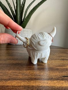 a small white elephant figurine sitting on top of a wooden table next to a potted plant