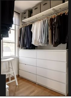 an organized closet with white drawers and clothes hanging on the rail, next to a window