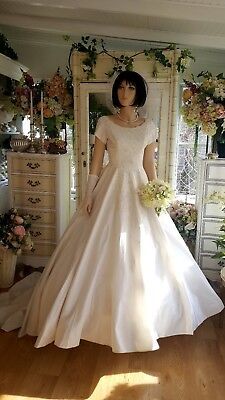 a mannequin wearing a wedding dress in a room with flowers on the wall