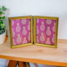 two framed pictures sitting on top of a wooden table next to a potted plant