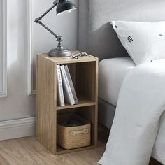 a bed with white sheets and pillows next to a night stand on wooden flooring