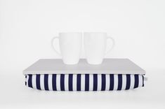 two coffee mugs sitting on top of a blue and white striped pillow next to each other