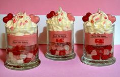 three small glass jars filled with different types of candy and marshmallows on a pink surface