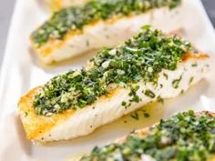 four pieces of fish covered in herbs on a white plate