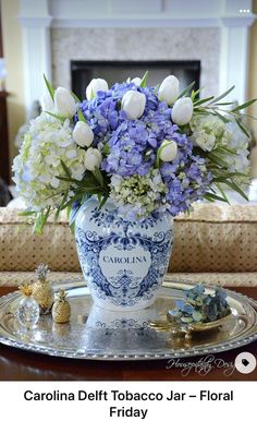 a blue and white vase filled with flowers on top of a silver tray next to a fireplace