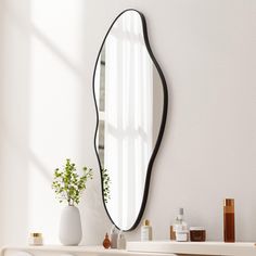 a mirror sitting on top of a white shelf next to a vase and potted plant