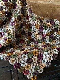 a crocheted blanket sitting on top of a wooden dresser next to a wall