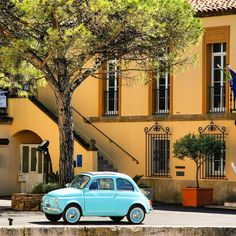 an old blue car parked in front of a yellow building