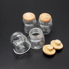 three glass jars with wooden lids on a black surface next to some cut up pieces of wood