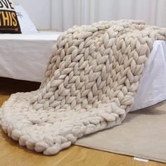 a large chunky blanket sitting on top of a wooden floor next to a bed