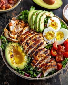 a salad with chicken, avocado, tomatoes and sliced eggs on the side