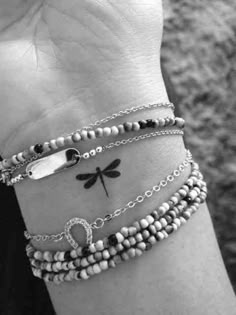 a woman's arm with three bracelets and a dragonfly tattoo on it