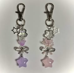 two key chains with charms attached to them on a white surface, one is pink and the other is purple