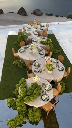 a long table set up with white plates and place settings for an outdoor dinner party