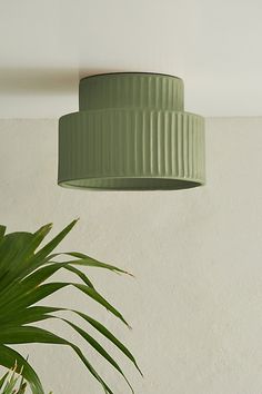 a green lamp hanging from the ceiling next to a potted plant