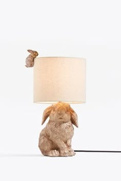 a rabbit lamp sitting on top of a table next to a white light fixture with a beige shade