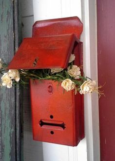 a red mailbox with flowers hanging from it's side on a door way