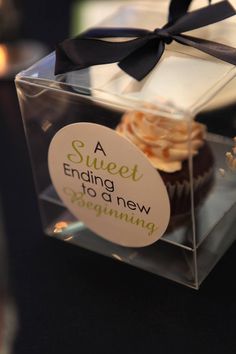 a cupcake in a clear box with a black bow on the top that says a sweet ending to a new beginning