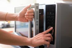 a woman is pressing the button on a microwave oven with both hands and touching it