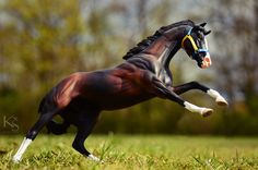 a toy horse standing on its hind legs in the grass with trees in the background