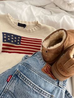 an american flag sweater, jeans and u s slippers are laid out on a bed