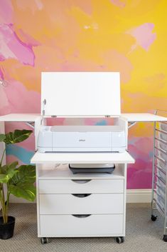 a white printer sitting on top of a desk next to a potted plant